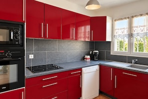 A kitchen with red cabinets, a black stove, a dishwasher, and a window with curtains.