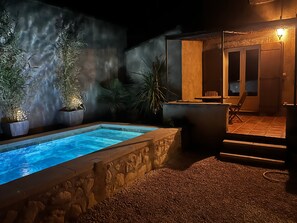 Une piscine bordée de pierres, entourée de plantes en pot et d’un mur de pierres.