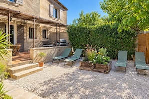 A patio with outdoor furniture, a barbecue grill, and a garden area with plants and a tree.