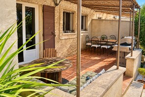 Une terrasse extérieure avec une table et des chaises en bois rondes, un barbecue et une pergola.