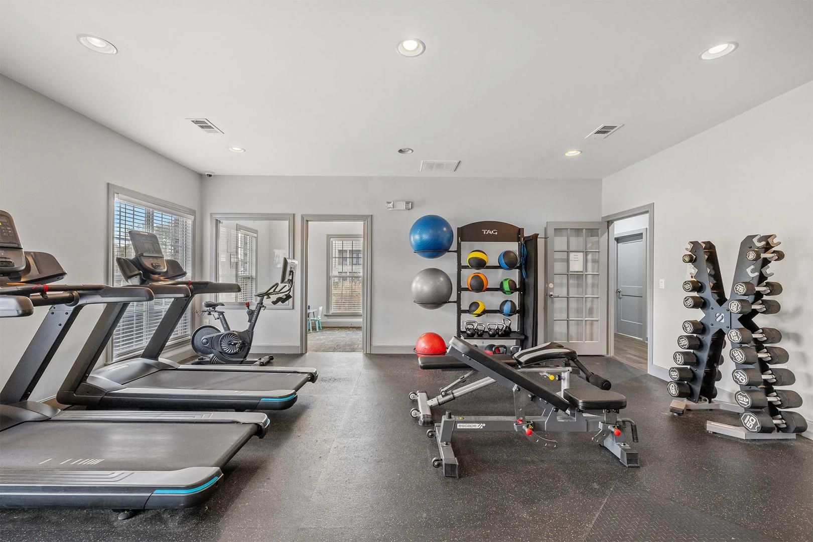 A gym with treadmills, a stationary bike, a bench press, and a rack of dumbbells.