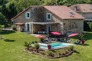 Una casa de piedra con piscina, mobiliario de exterior y jardín.