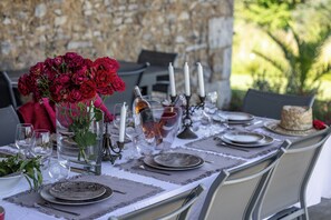 A table set for dining outdoors with a stone wall backdrop, clear glassware, and a vase of red flowers. - New Listing (Milhac-de-Nontron)