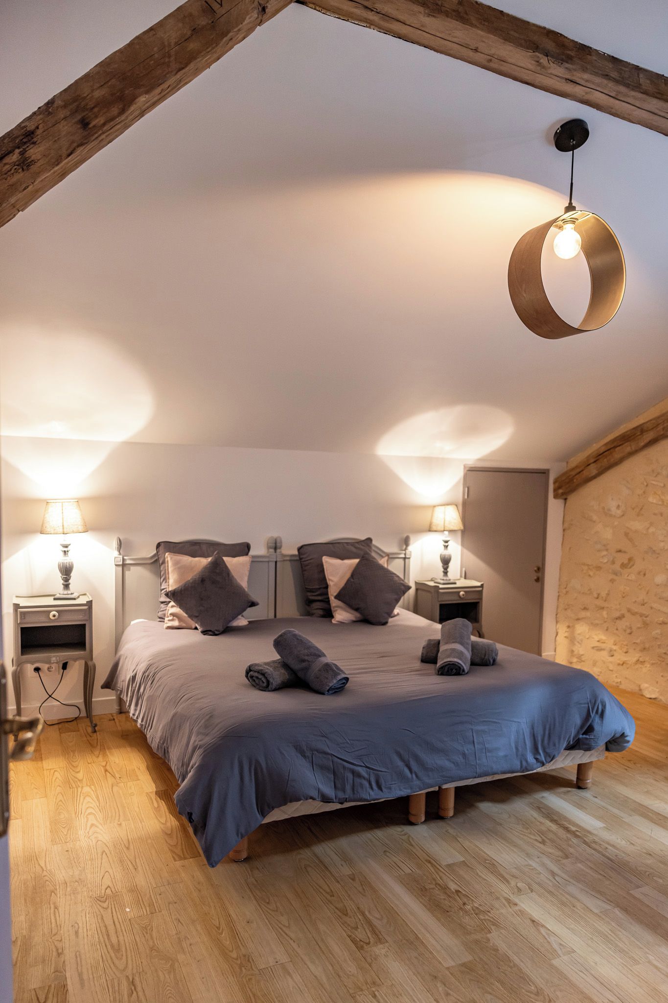 A bedroom with a sloped ceiling, a bed with pillows and towels, two bedside lamps, and a hanging light fixture.