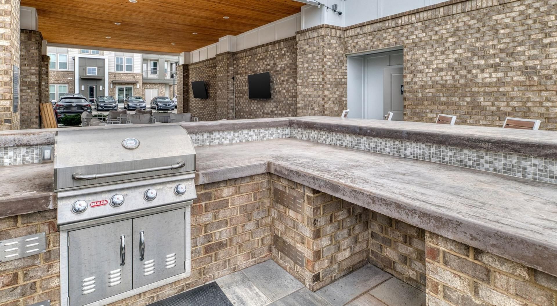 An outdoor kitchen area with a grill, built-in seating, and a brick wall.