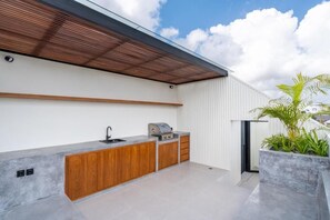 Une cuisine extérieure équipée d’un barbecue, de meubles en bois et d’un plan de travail en béton.