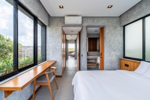 Une chambre d’hôtel moderne avec un grand lit, un bureau et une vue sur la verdure environnante.