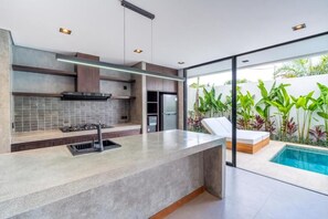 A modern kitchen with a large island, built-in appliances, and a view of a swimming pool. - Ave Fenix 2BR Villas Balangan (Jimbaran)
