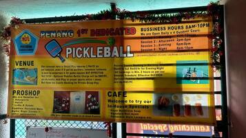 A pickleball court sign with business hours, venue details, and a pro shop listing sports equipment.