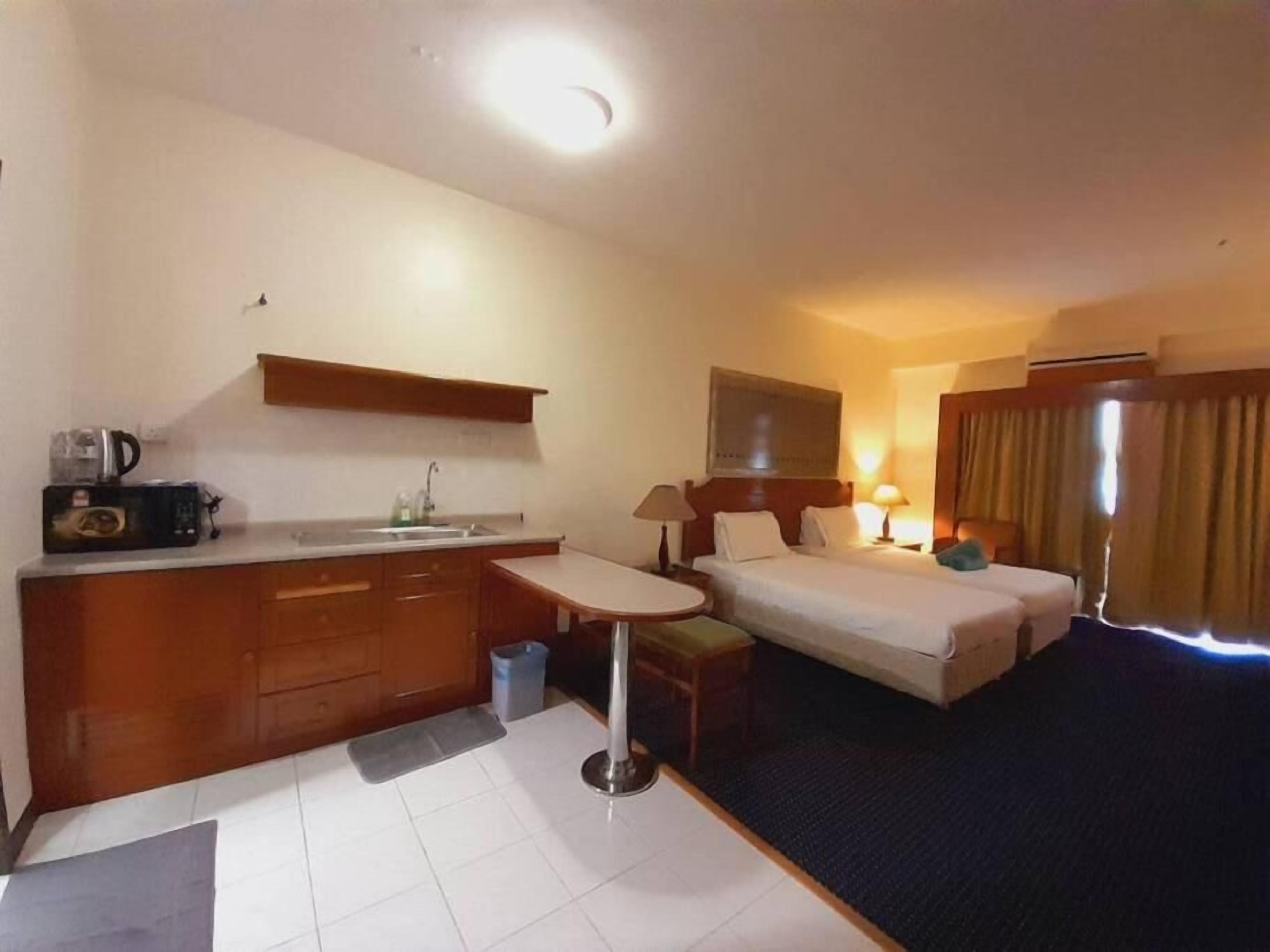 Ett hotellrum med en säng, ett skrivbord, en stol, ett litet bord, ett handfat och en spegel.