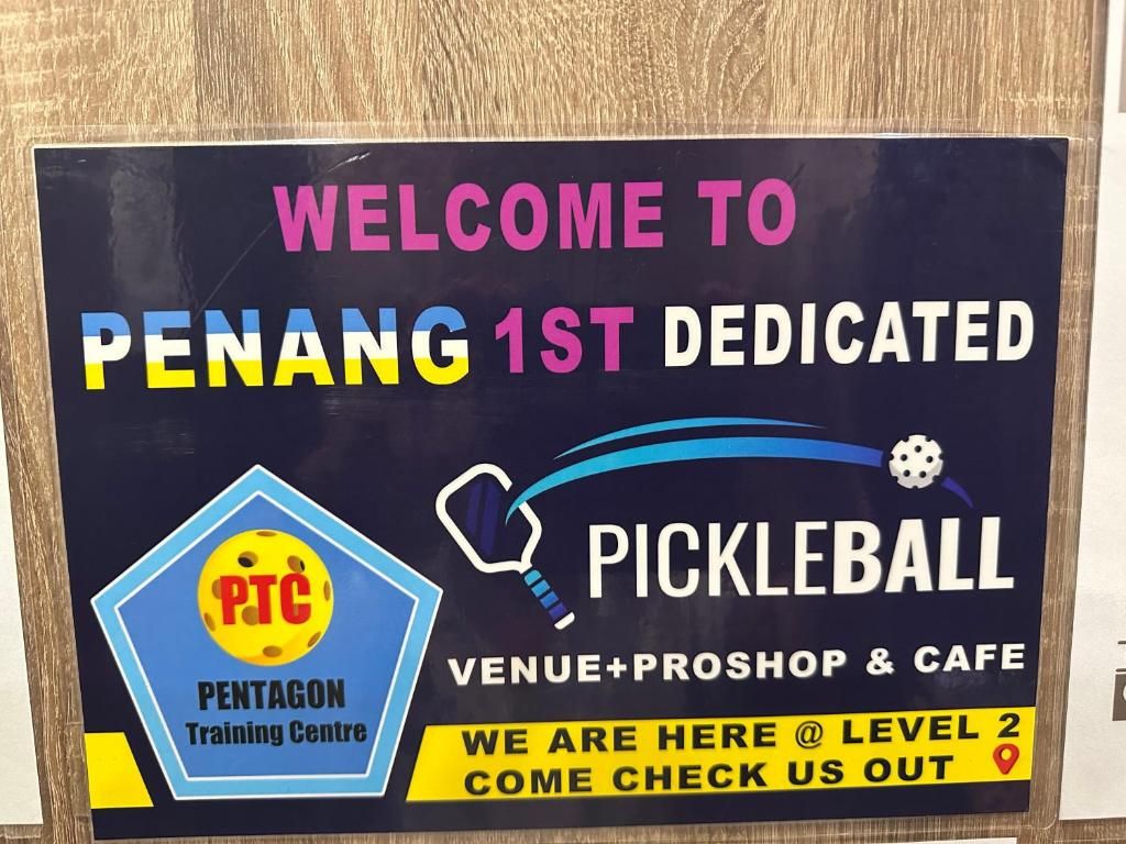 A welcome sign for Penang 1st Dedicated Pickleball venue, including a pentagon logo and a location marker.