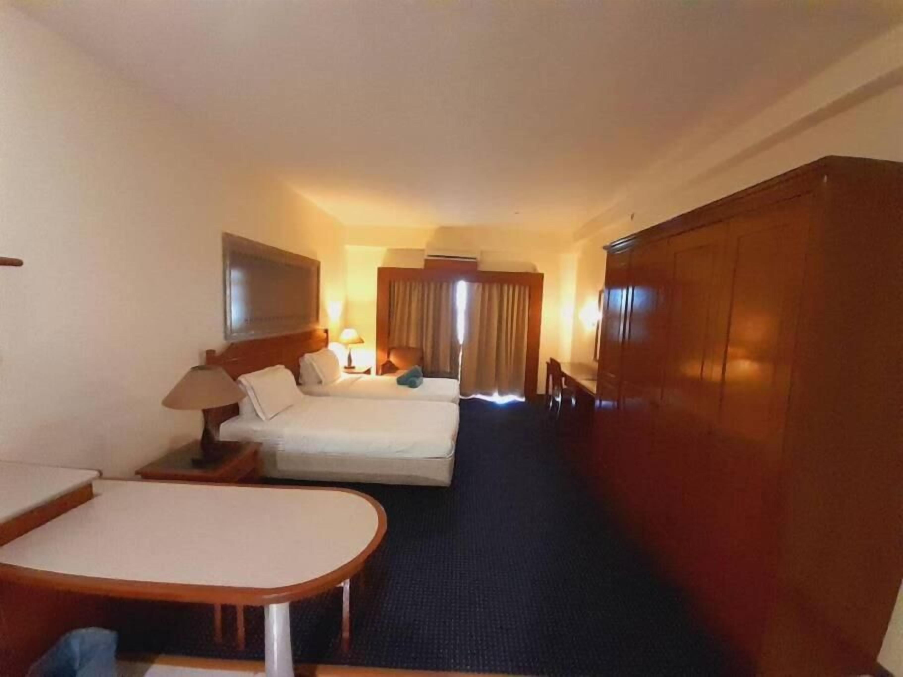 A hotel room with a bed, a desk, a chair, a wardrobe, and a television.