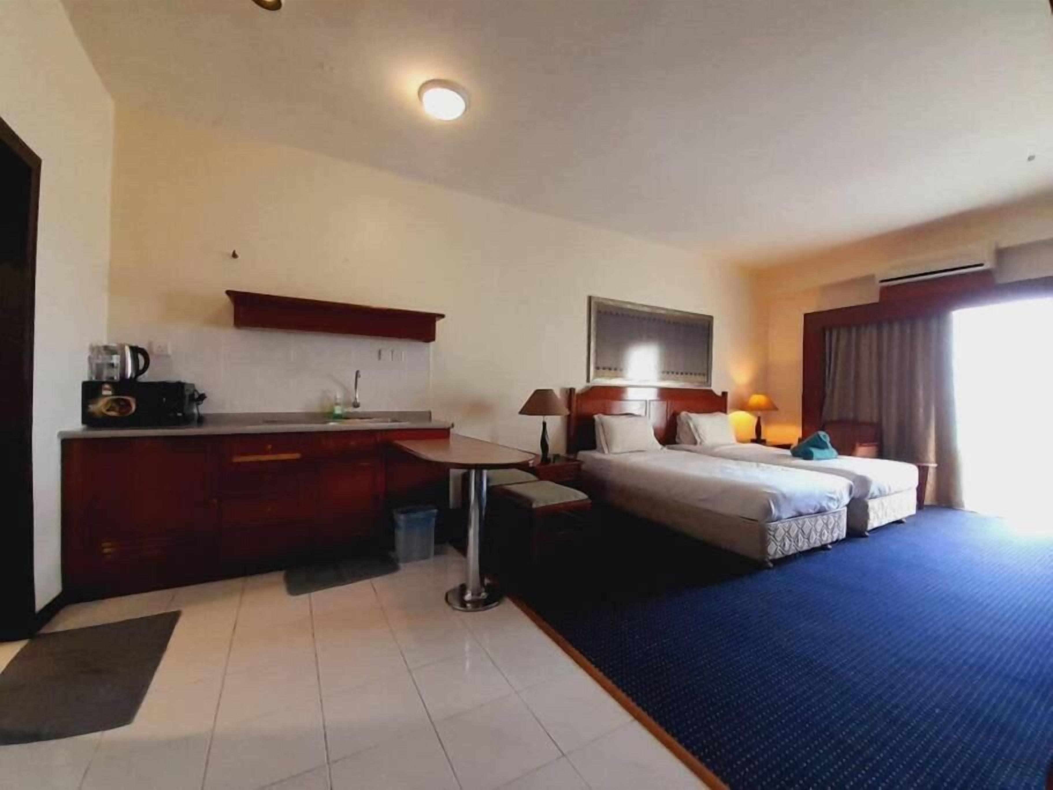 A hotel room with a bed, a desk, a small kitchenette, and a window.