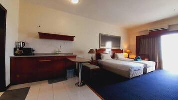A hotel room with a bed, a desk, a small kitchenette, and a window.