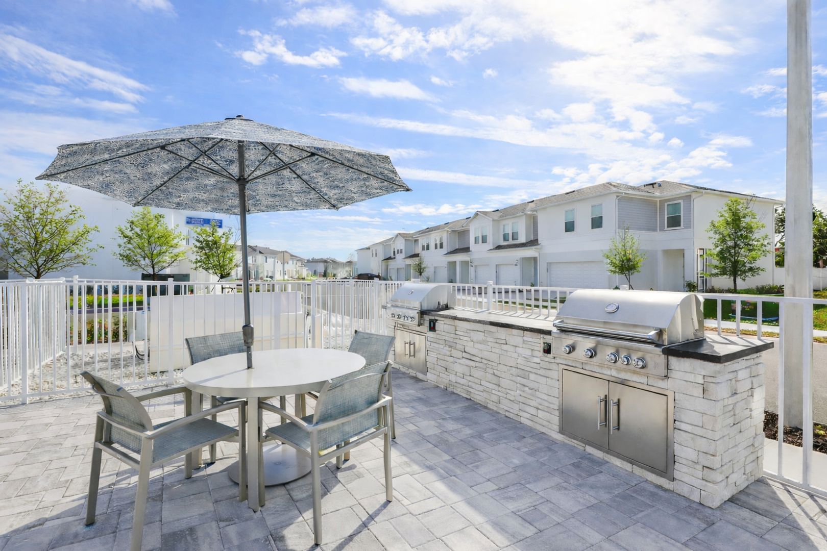 An outdoor patio with a round table, chairs, an umbrella, and a built-in barbecue grill.