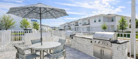 An outdoor patio with a round table, chairs, an umbrella, and a built-in barbecue grill.