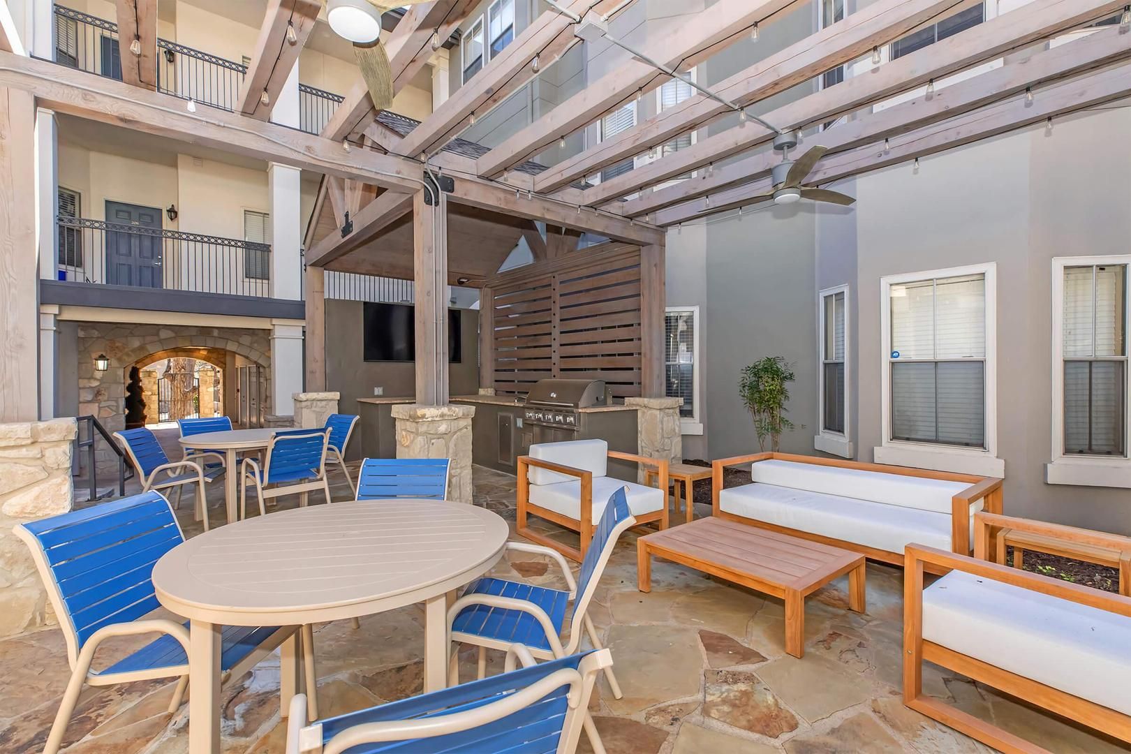 An outdoor patio with a stone floor, wooden furniture, and a grill area.