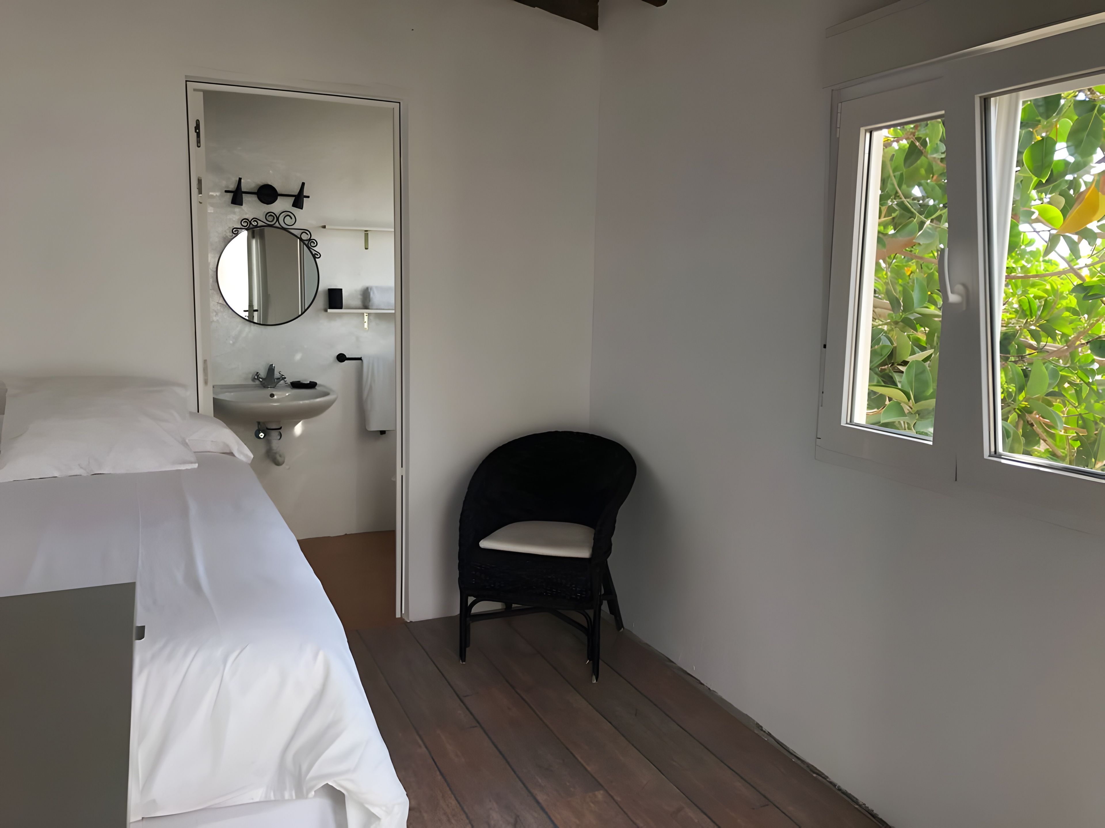 Een slaapkamer met een bed, nachtkastje, stoel, raam en spiegel.