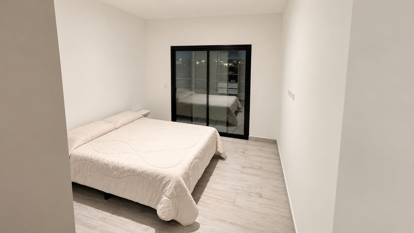A bedroom with a bed, a nightstand, and a sliding glass door leading to a balcony.