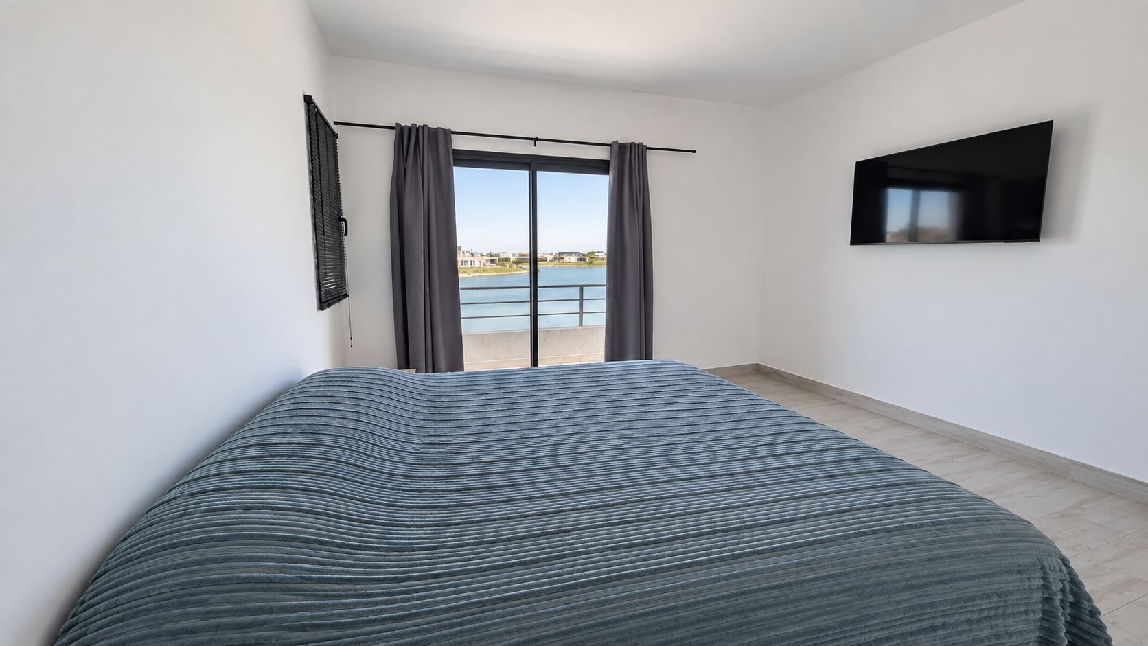 A bedroom with a bed, a TV, a window with curtains, and a view of a body of water.