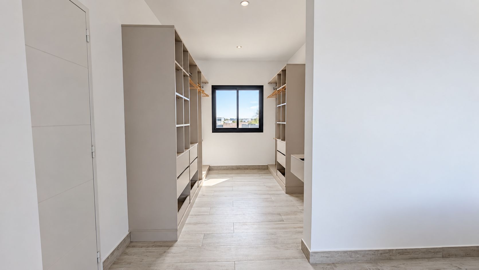A corridor with built-in shelving units on both sides, leading to a window with a view of buildings.