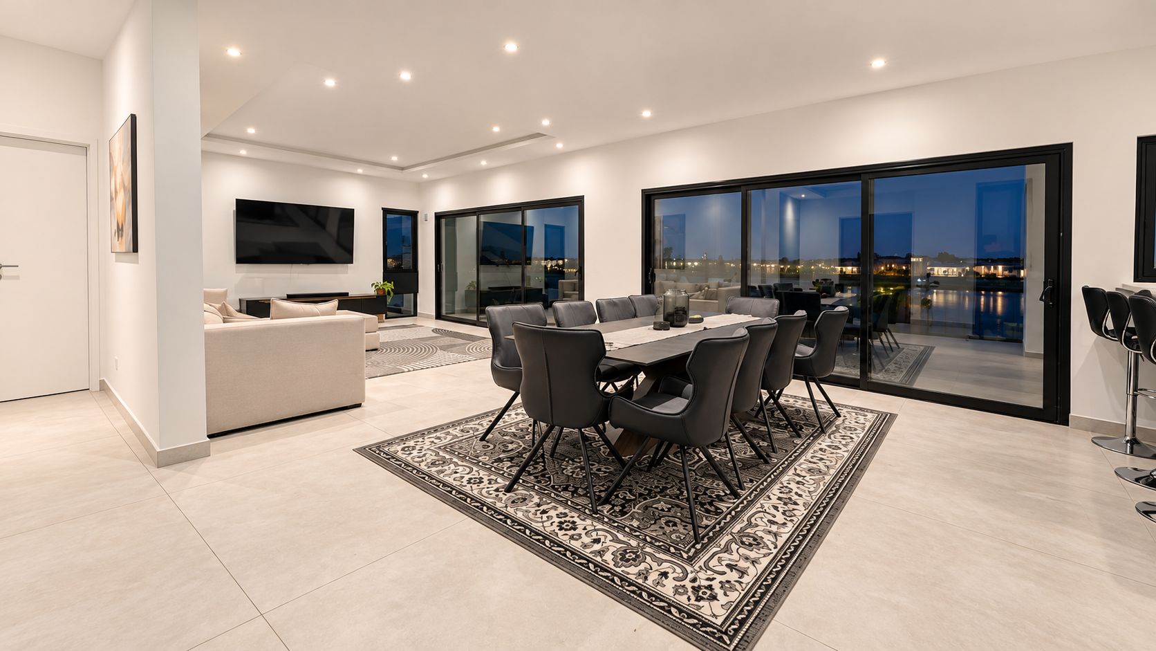 Un intérieur moderne comprenant un coin repas, un canapé, un téléviseur et une vue dégagée grâce à de grandes fenêtres.