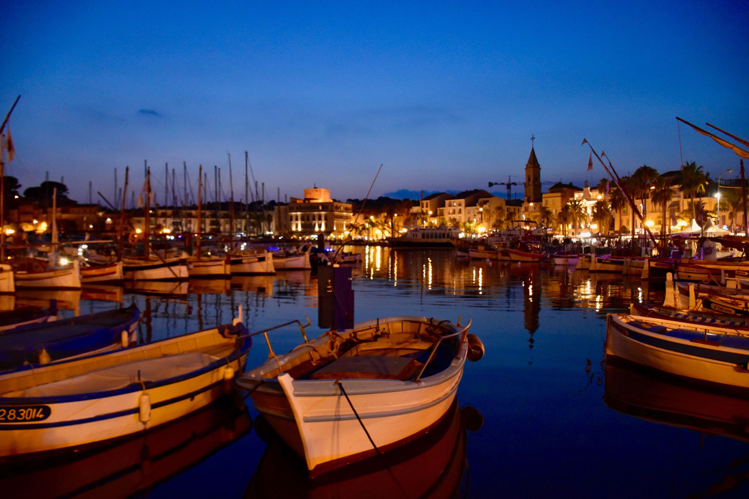 Ein Hafen im Abendlicht mit vertäuten Booten, ruhigem Wasser und Gebäuden im Hintergrund.