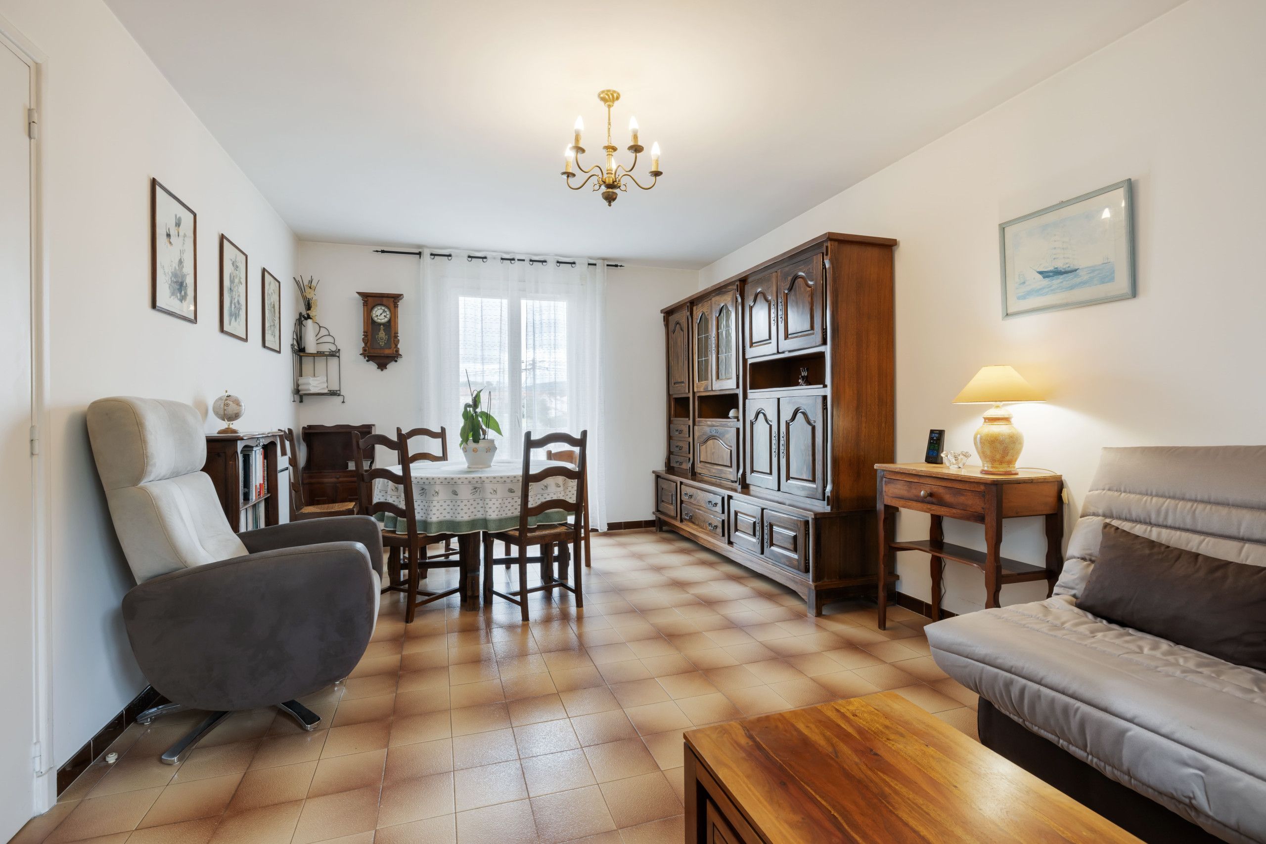 Een woonkamer met een bank, een salontafel, een eethoek met tafel en stoelen, een houten kast en een kroonluchter.