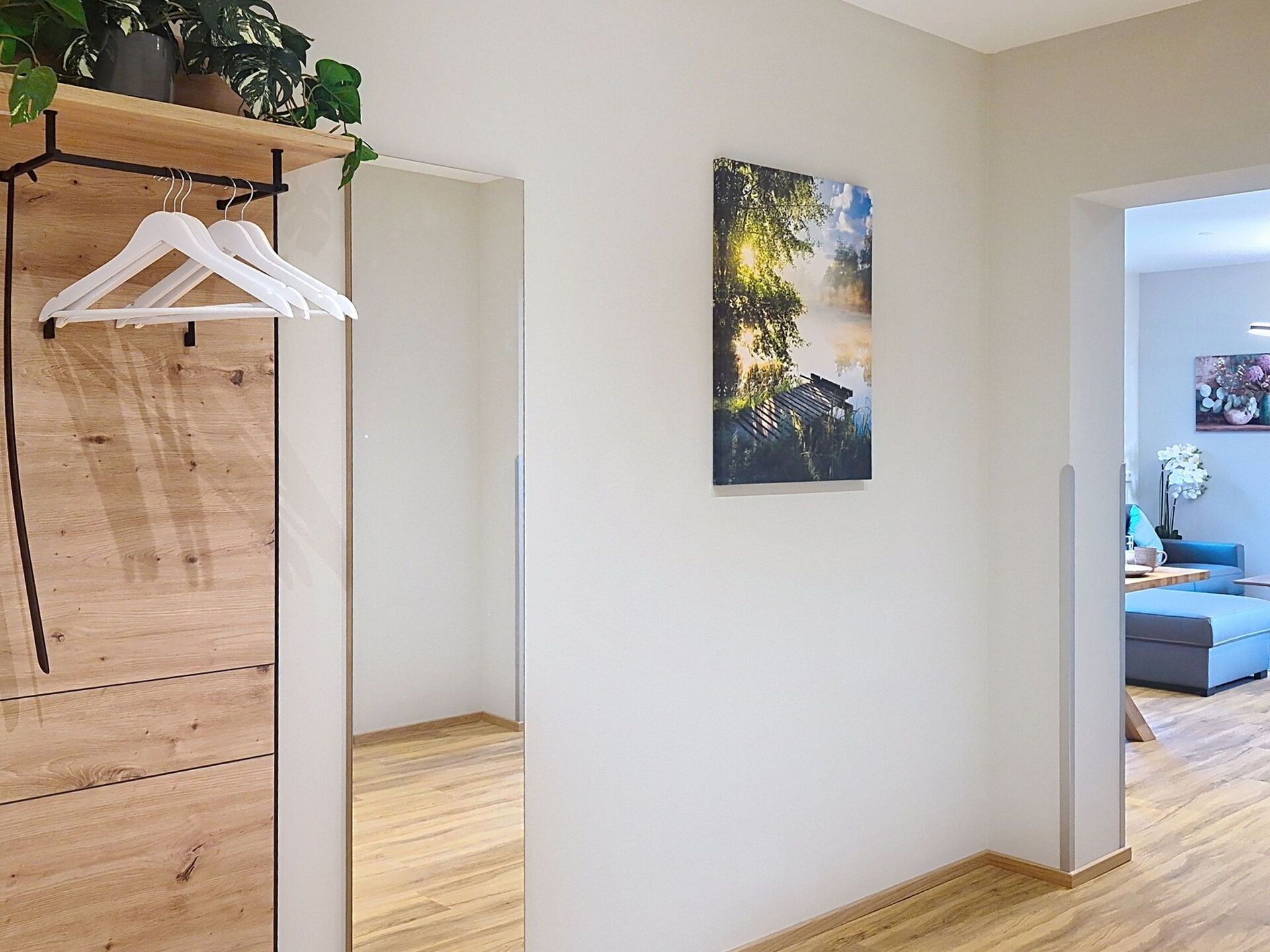 Una habitación con un armario de madera, un cuadro de un paisaje y un sofá azul al fondo.