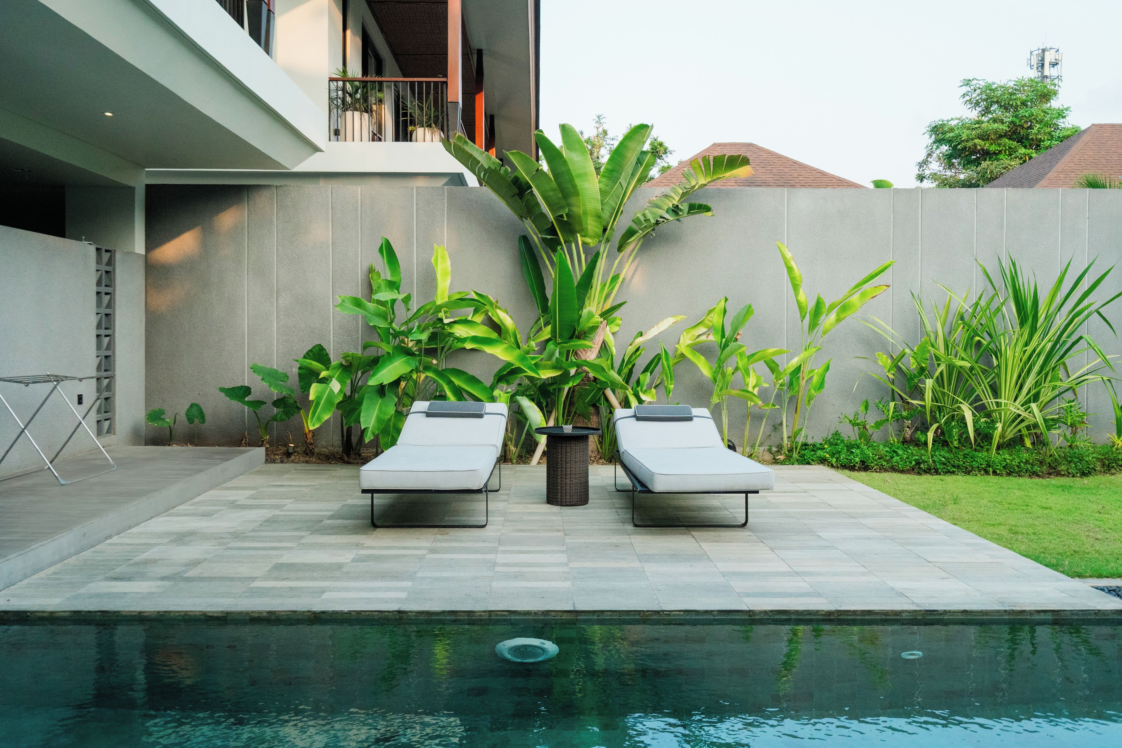 Een modern zwembadterras met twee ligbedden en diverse tropische planten.