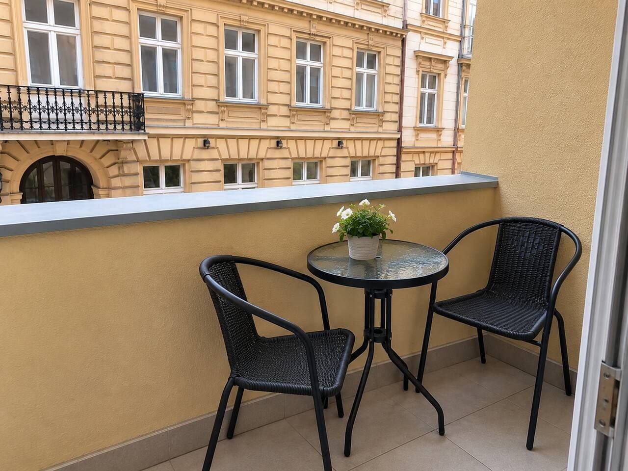 Ein Balkon mit zwei Stühlen, einem Tisch, einer Topfpflanze und Blick auf ein Gebäude mit vielen Fenstern.