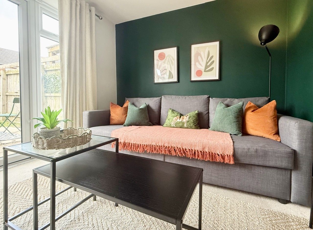 Ein Wohnzimmer mit einem grauen Sofa, einem schwarzen Couchtisch und einer grünen Wand mit zwei gerahmten Kunstwerken.