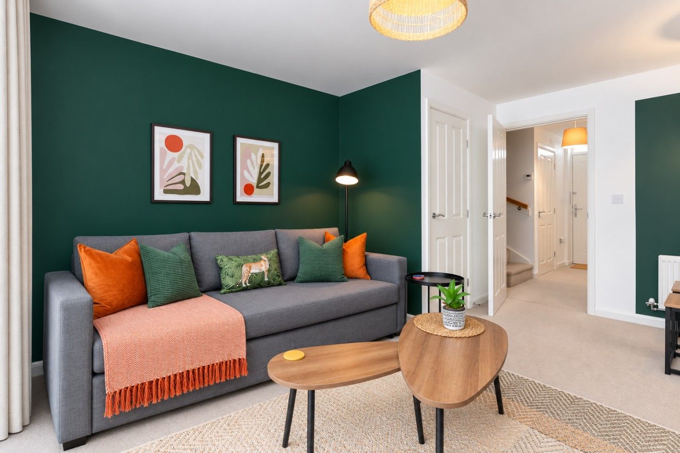 A living room with a grey sofa, orange and green cushions, a round wooden coffee table, and a floor lamp.