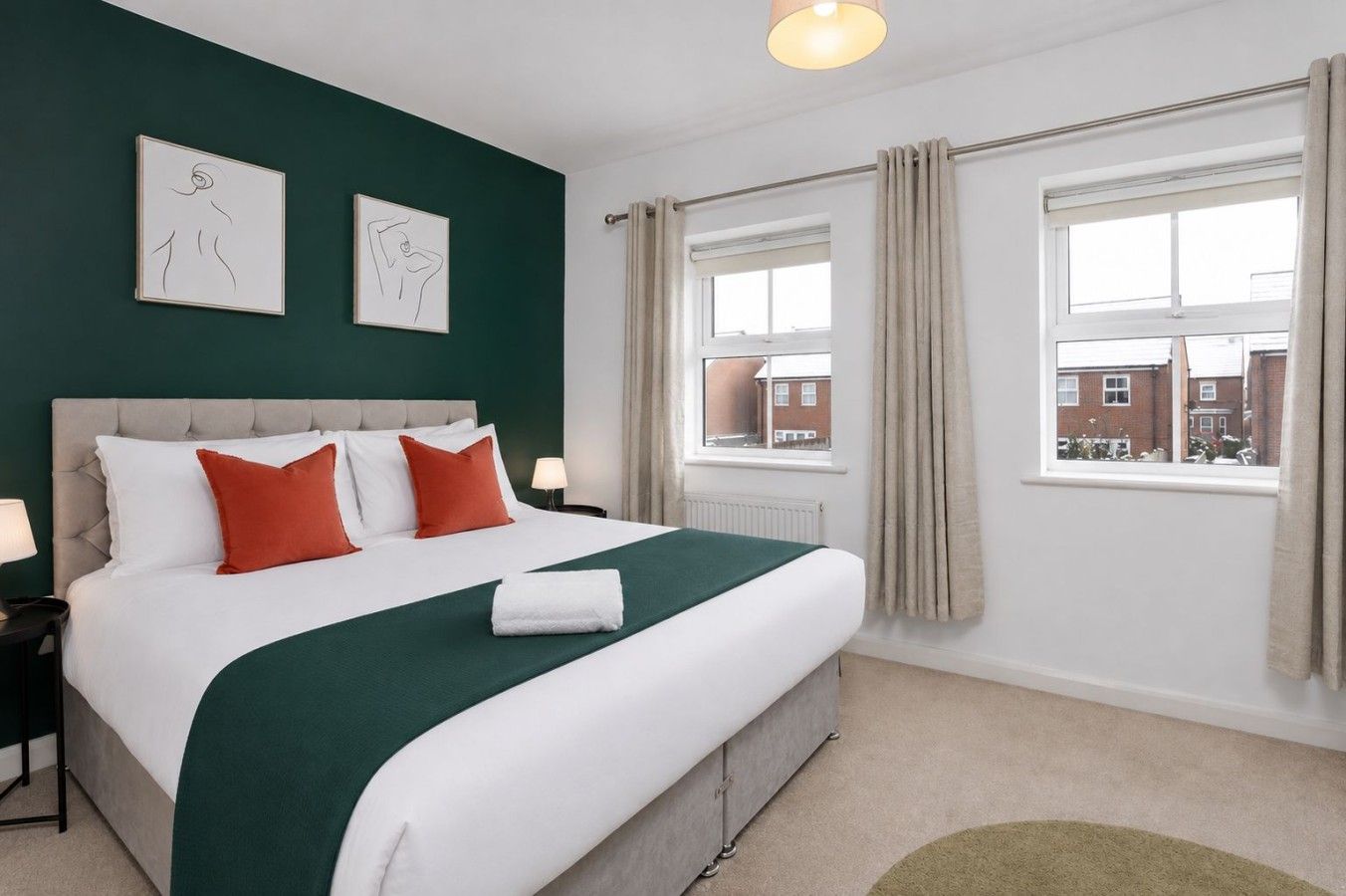 A hotel room with a large bed, two side tables, a window with curtains, and artwork on the wall.