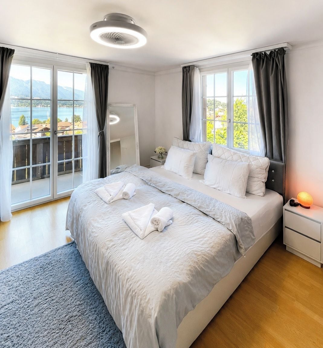 Een moderne slaapkamer met een groot bed, een nachtkastje, een lamp en uitzicht op het omliggende landschap.