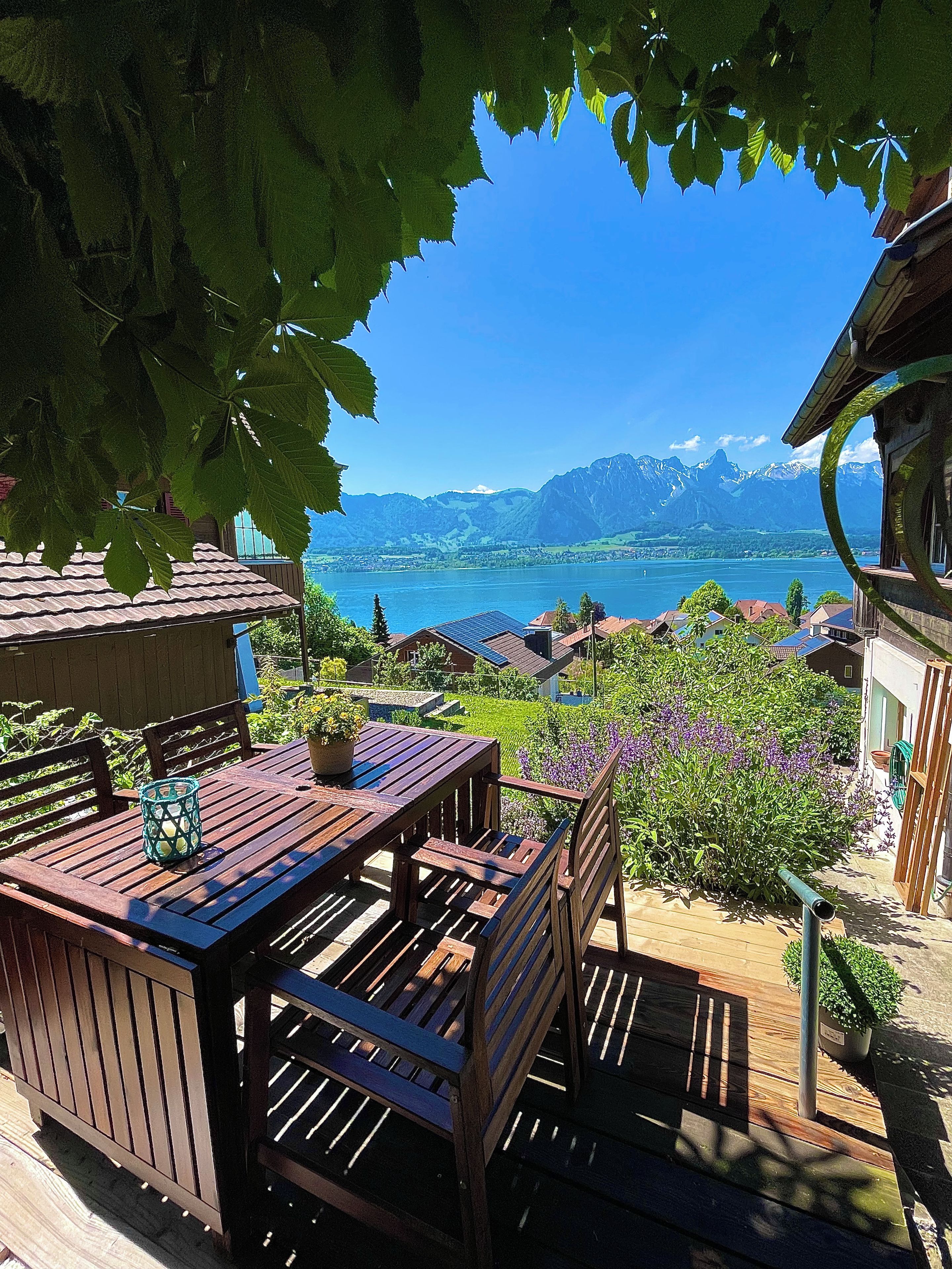 Une terrasse en bois avec une table et des chaises, donnant sur un lac avec des montagnes en arrière-plan.