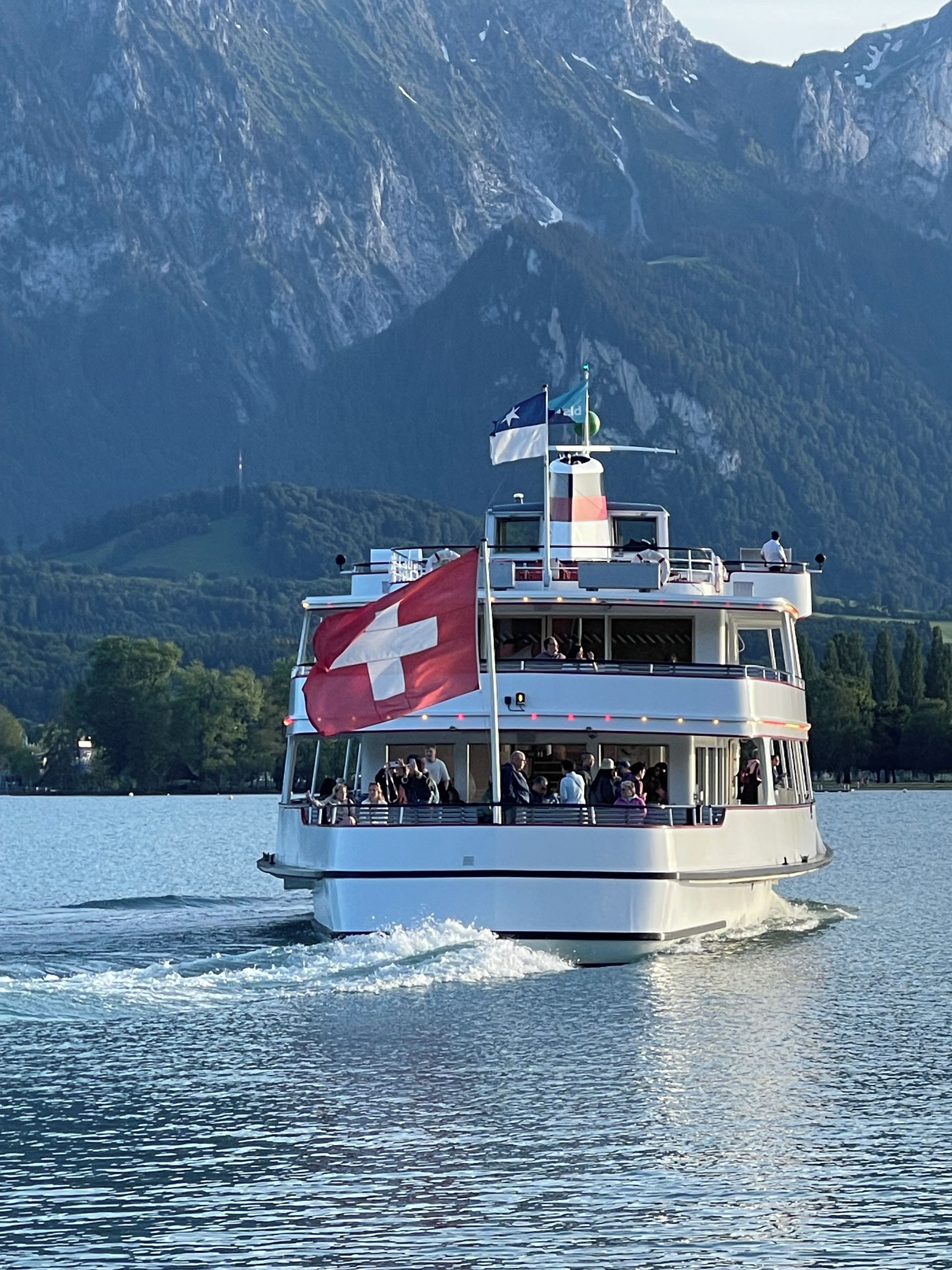 A boat with a Swiss flag, passengers, and a mountainous landscape in the background.