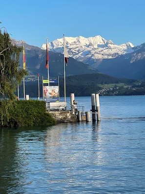 Un muelle junto al lago con banderas, un letrero de transporte lanzadera y montañas al fondo.