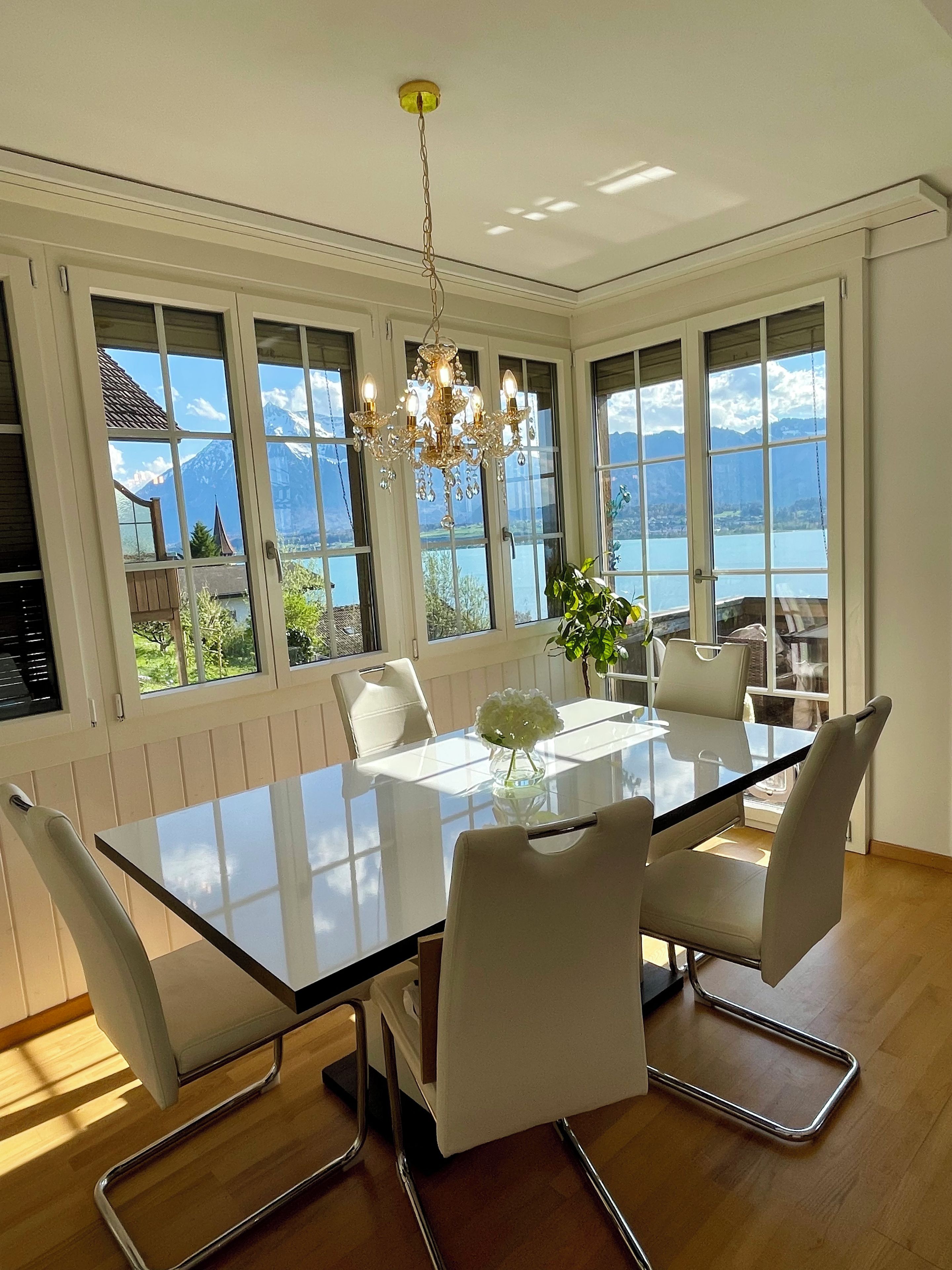 Un coin repas avec une table en verre, des chaises blanches et un lustre.