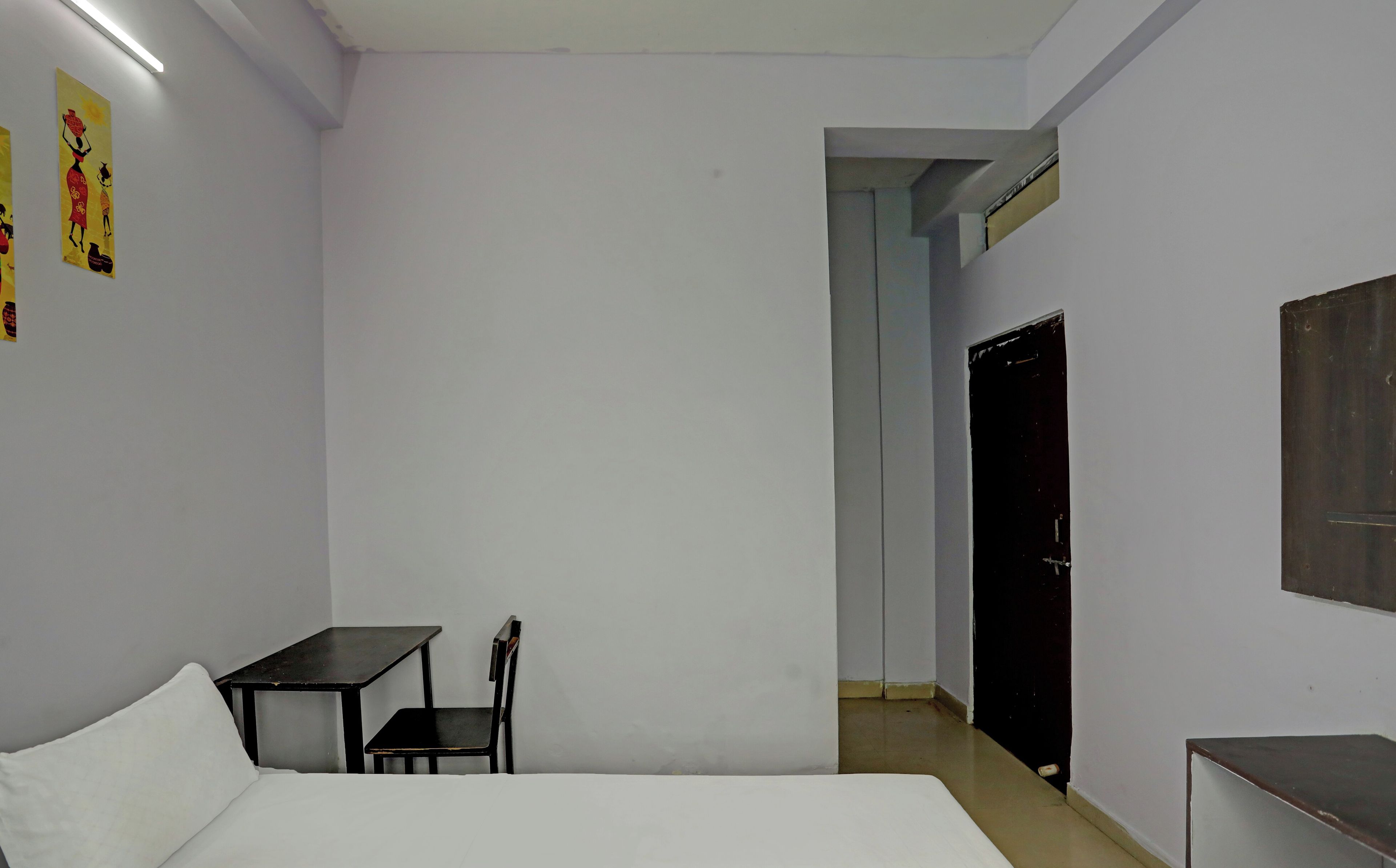 A room with a bed, a desk, and a chair. There is a door leading to another room.