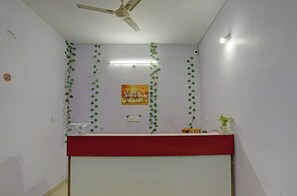 A room with a ceiling fan, a wall-mounted light, a red counter, and green leaf decorations. - Hotel O 815596 Hotel Sambodhi Palace (Bhopal)