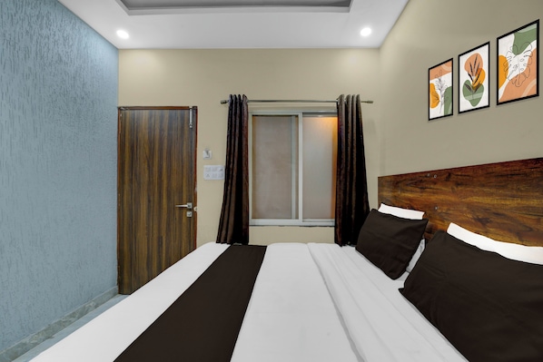 Habitación de hotel con cama, cabecero de madera, ventana con cortinas y una pared con obras de arte enmarcadas.