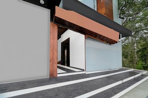 Un edificio moderno con una escalera que conduce a una puerta, rodeado de vegetación.