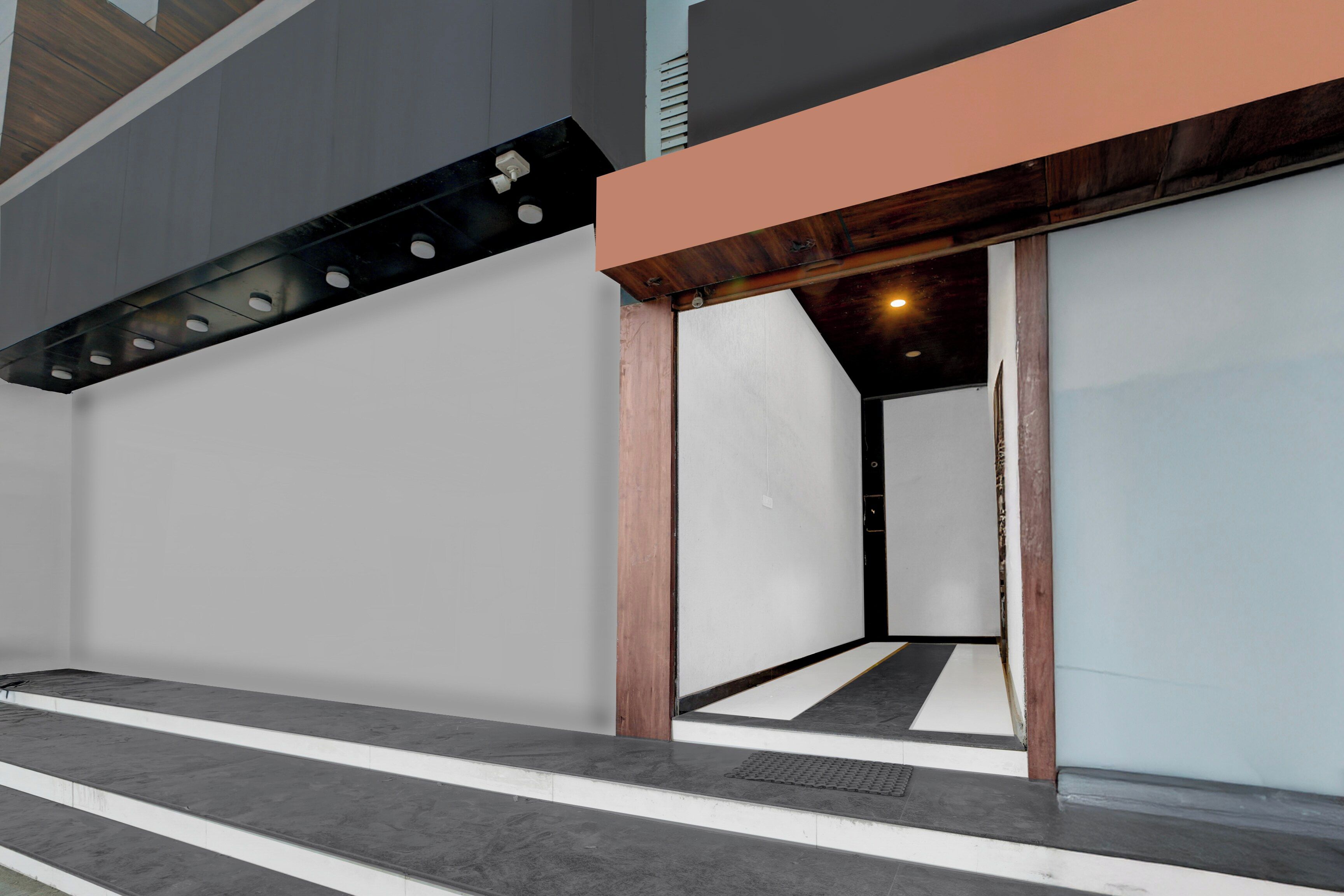 Entrada de un edificio moderno con una rampa de hormigón que lleva a una puerta, un alero de madera sobre la puerta y una rejilla de ventilación en la pared.