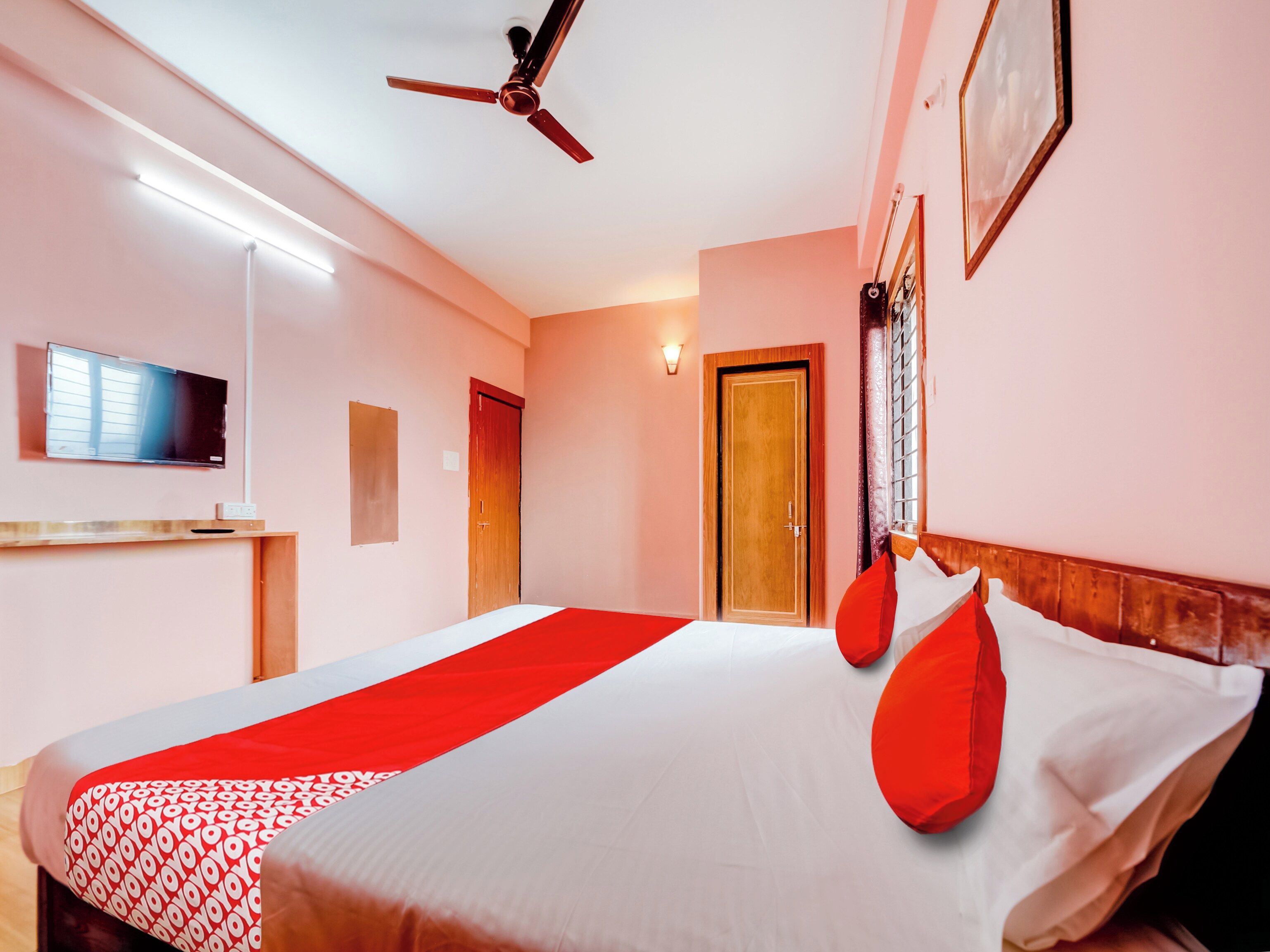 A hotel room with a bed, a ceiling fan, a TV, and a door.