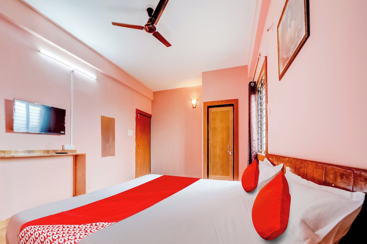 A hotel room with a bed, a ceiling fan, a TV, and a door.
