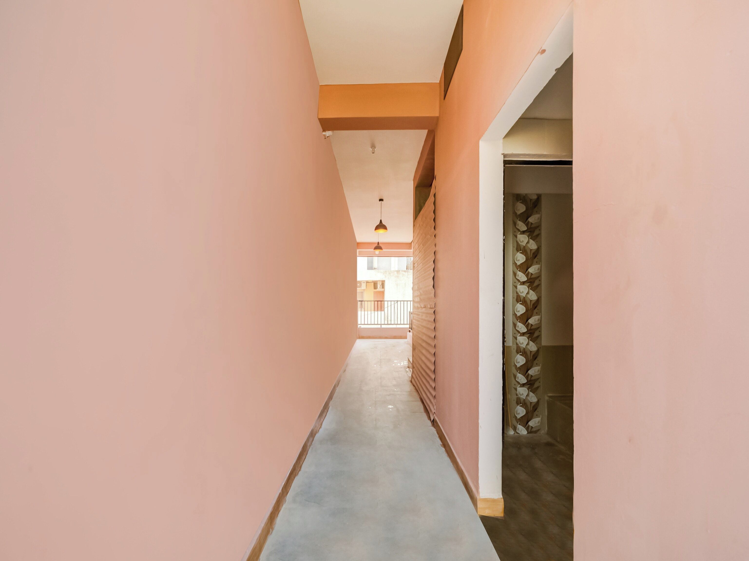 A corridor with a concrete floor and pink walls, leading to a room with a white door and a decorative wall.