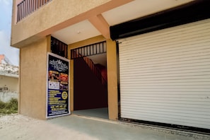 A hotel entrance with a closed shutter, a staircase leading to an upper floor, and a signboard advertising amenities like AC rooms, banquet hall, and free WiFi. - Hotel O Crown Square (Bhopal)