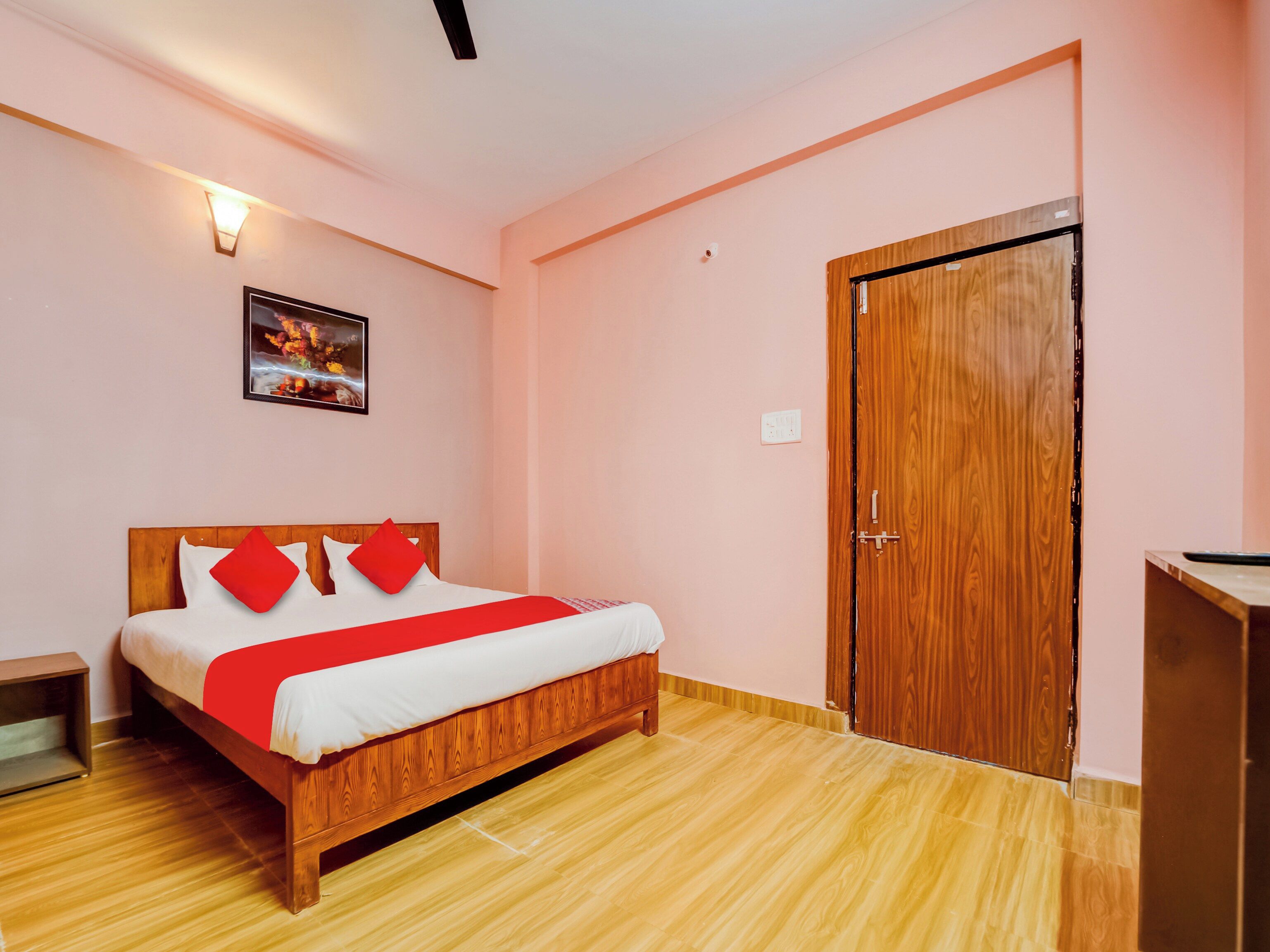 A hotel room with a wooden bed, a red and white bedspread, a wooden wardrobe, and a wall-mounted light fixture.