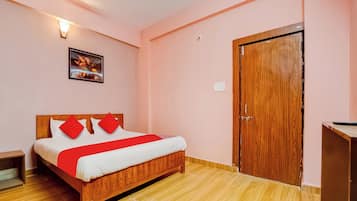 A hotel room with a wooden bed, a red and white bedspread, a wooden wardrobe, and a wall-mounted light fixture.